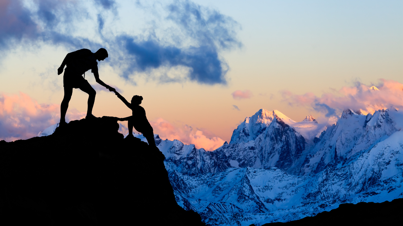 a mountain climber extends a hand to help a fellow climber to the peak at sunrise